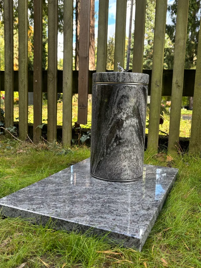 Dunkle Natursteinurne vor dem Holzzaun